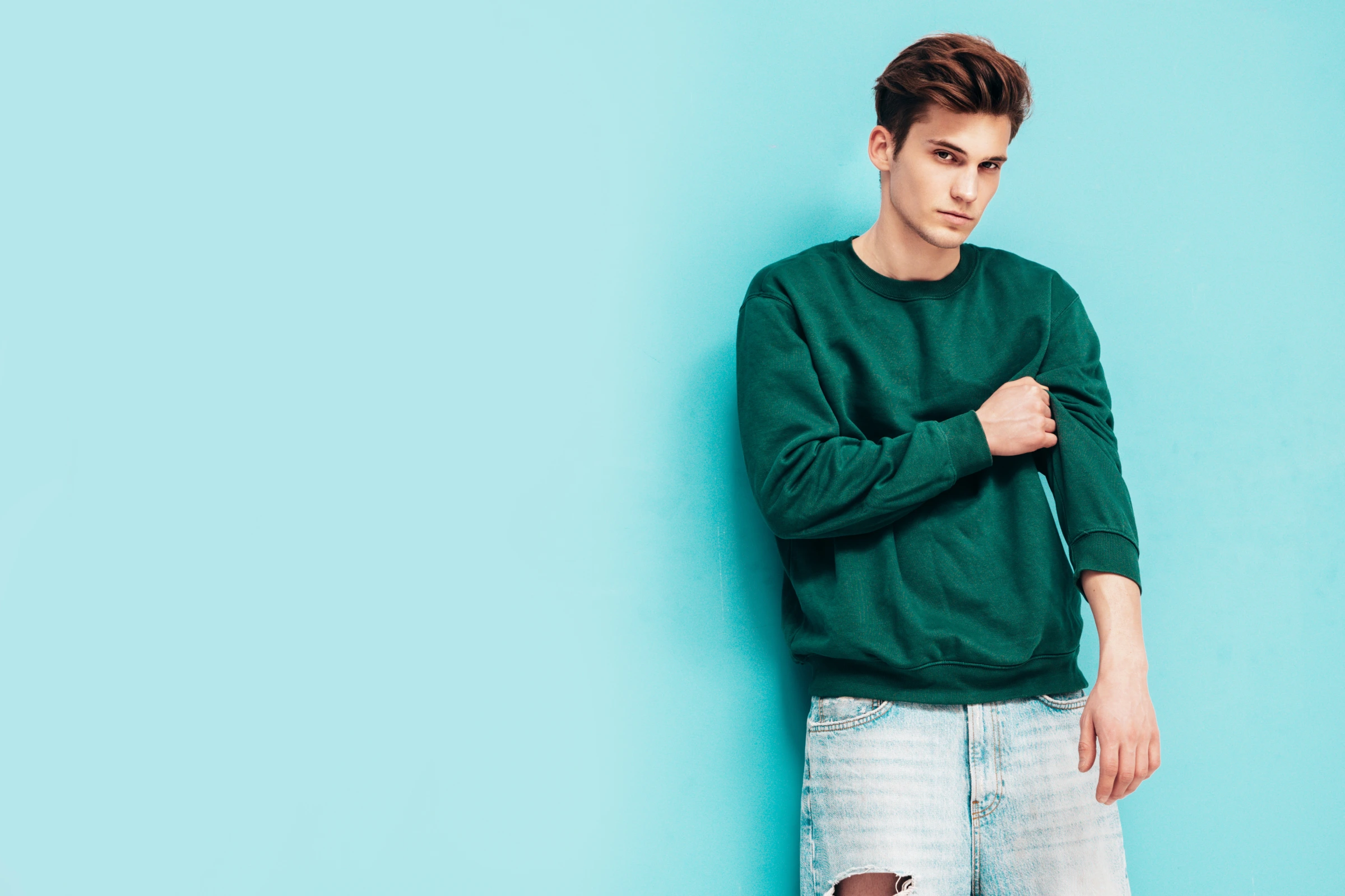portrait-handsome-confident-stylish-hipster-lambersexual-modelman-dressed-green-sweater-jeans-fashion-male-posing-studio-near-blue-wall